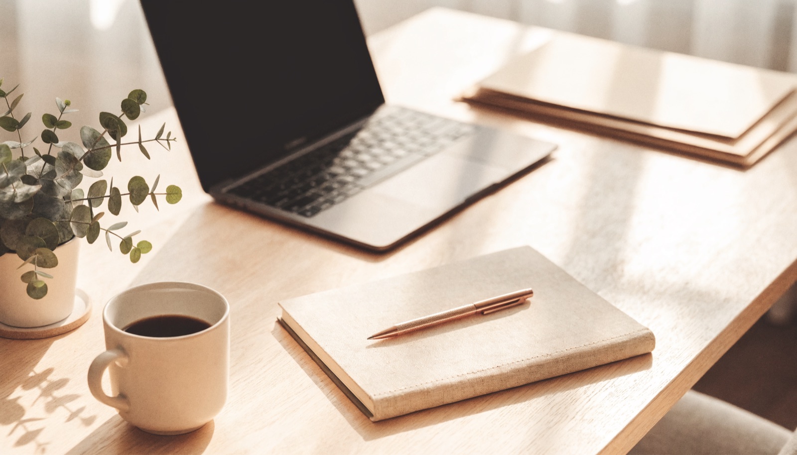 Heller Schreibtisch mit Laptop, Notizbuch und Kaffeetasse im Tageslicht